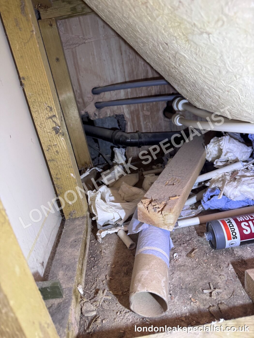 Supply and waste pipework visible in a small access opening beside a bath