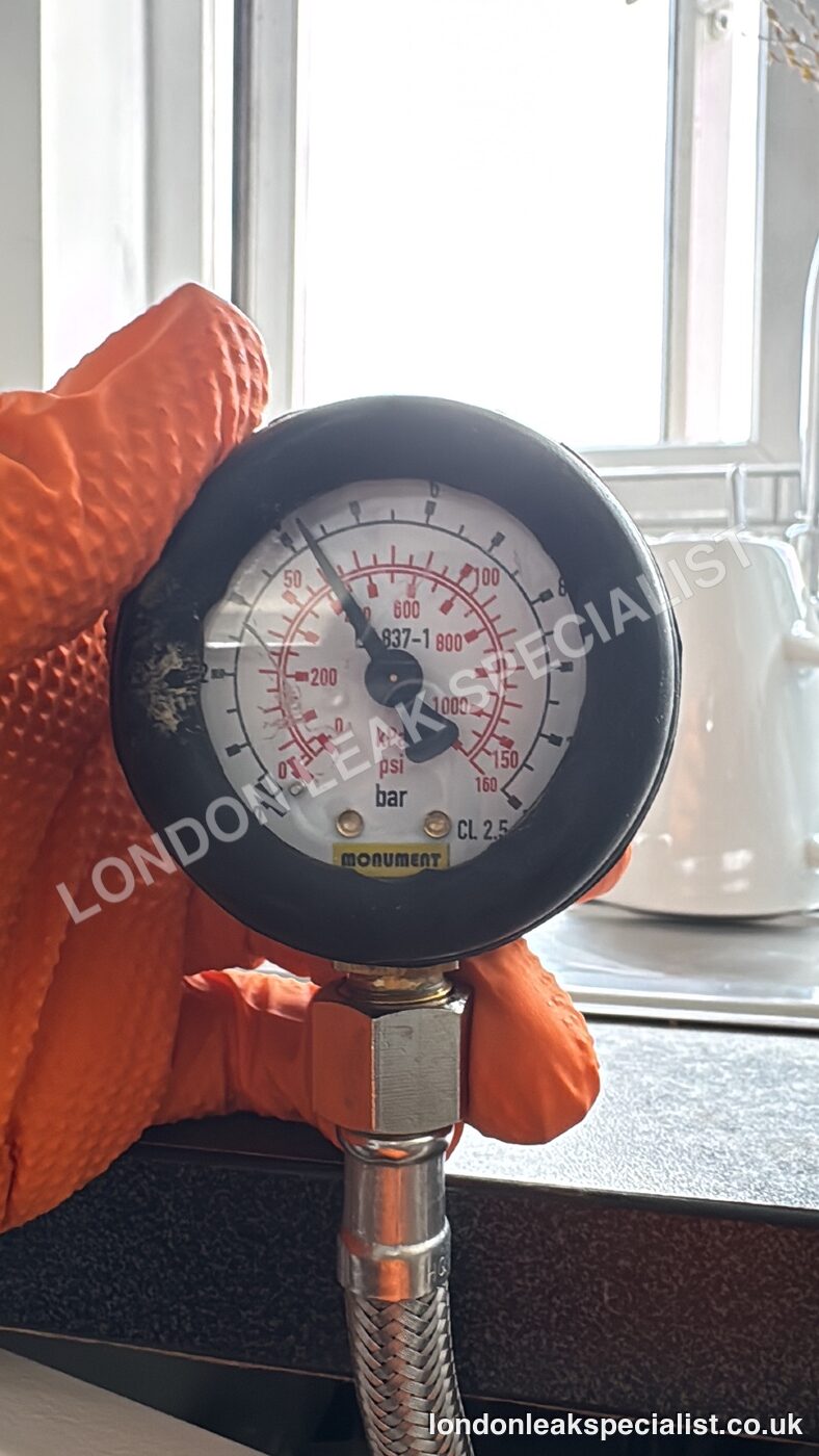 A pressure gauge held in an orange glove during a hot and cold water pressure test