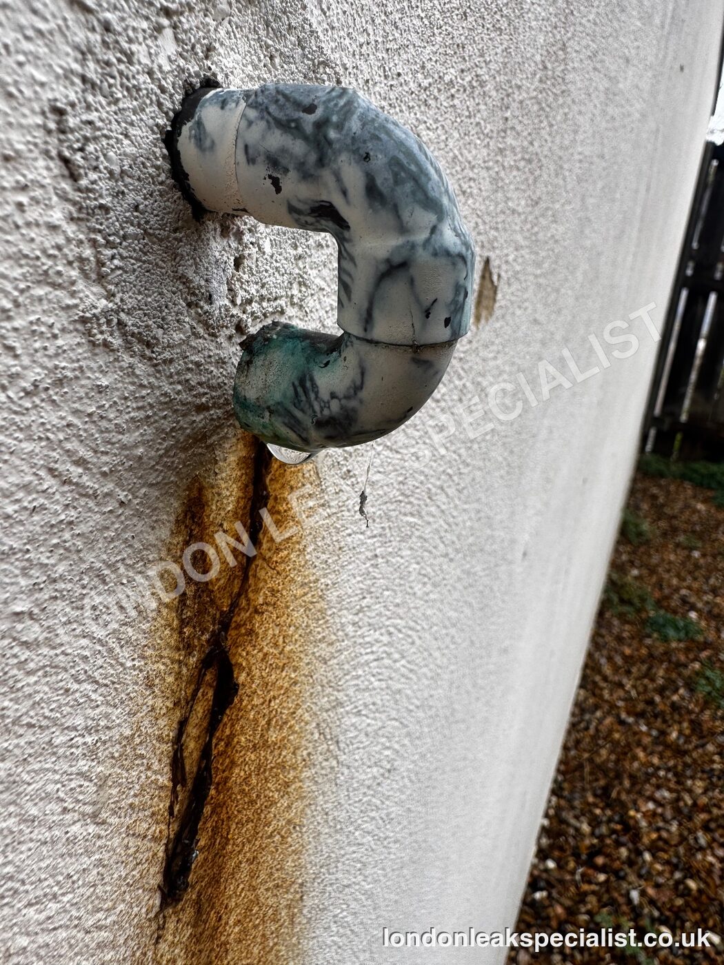 A pressure relief valve discharge pipe on an external rendered wall with a rust streak running down the render beneath it