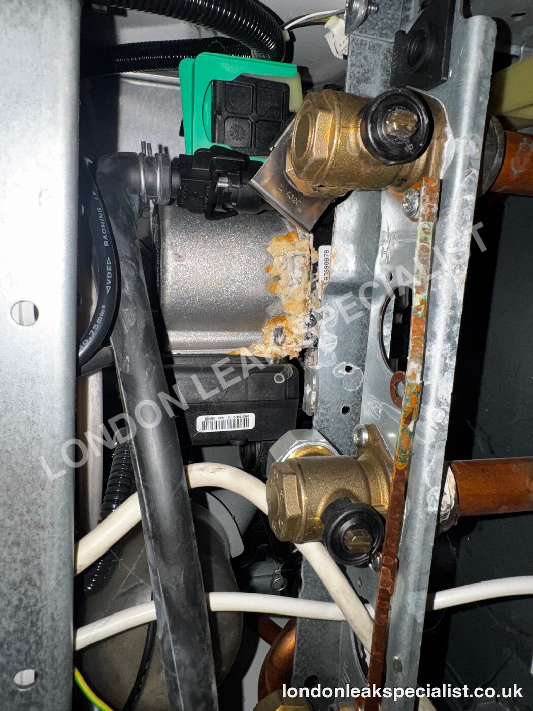 Brass fittings and a deposit of orange limescale and corrosion inside the casing of a boiler