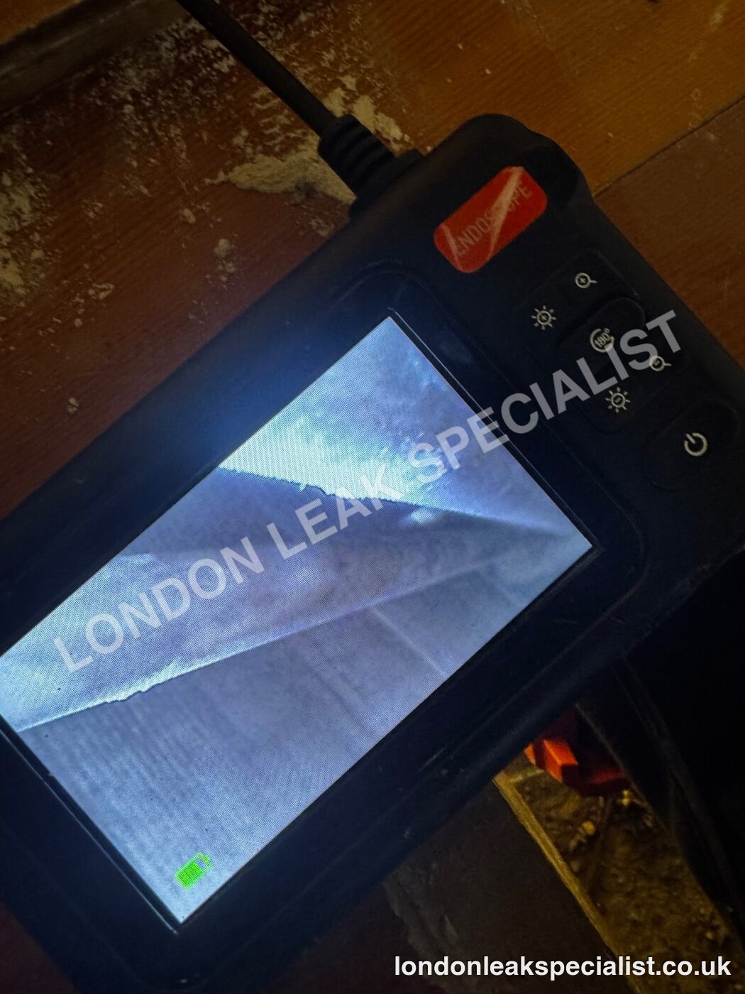 An endoscope monitor showing the view into a floor void beside a timber surface