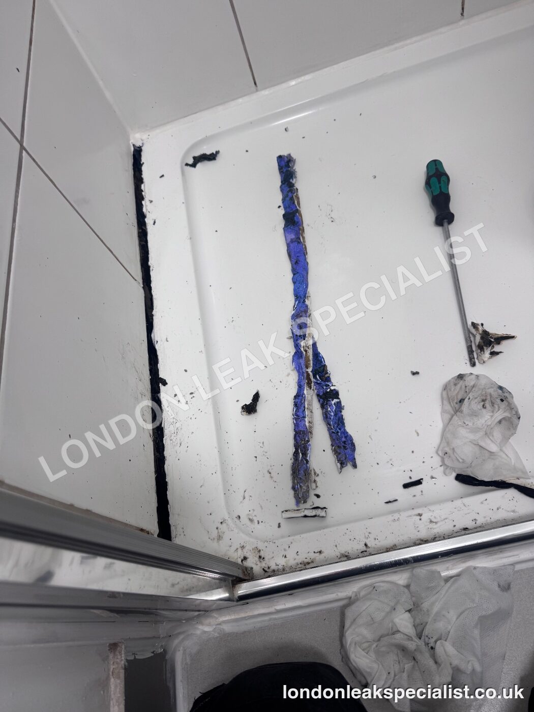 Blue tracer dye marks on the base of a shower tray beside a screwdriver