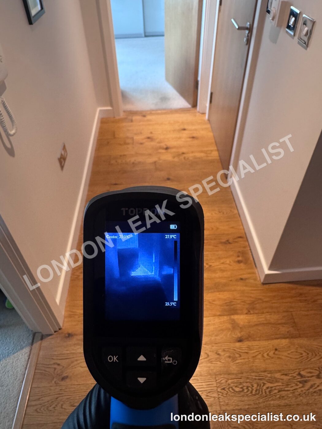 A thermal imaging camera held in a hallway pointing along a timber floor