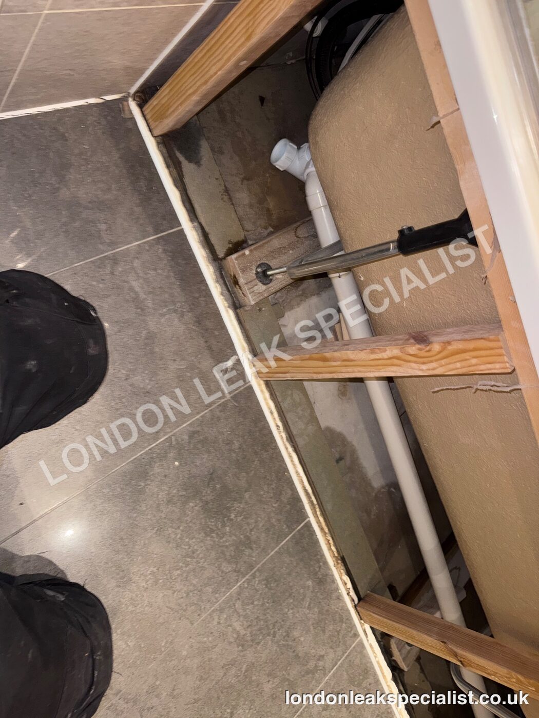 An opened panel beside a bath showing a white pipe and timber framing