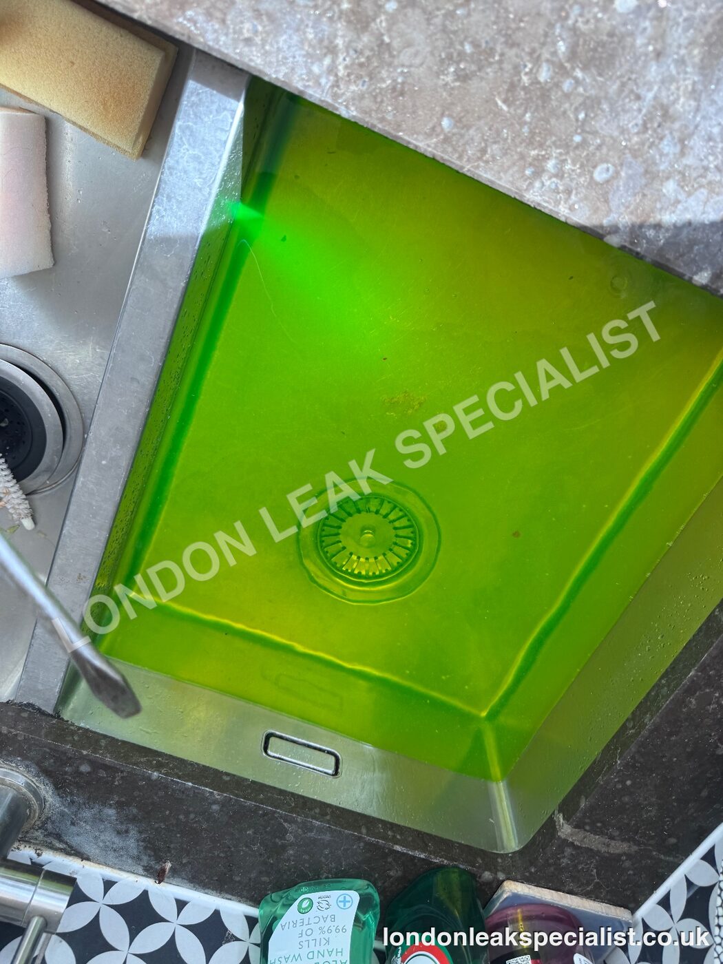 Bright green tracer dye filling a stainless steel kitchen sink during a drainage test